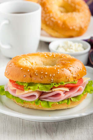 Bagel sandwich with ham, cheese, tomato, green salad lettuce, tea, delicious breakfastの写真素材