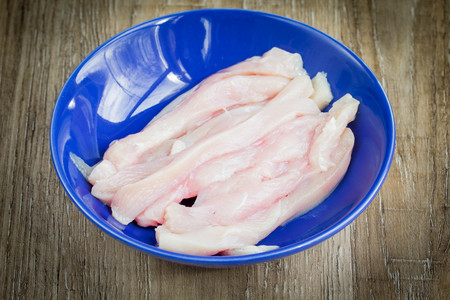 Raw slices of chicken in blue bowlの写真素材