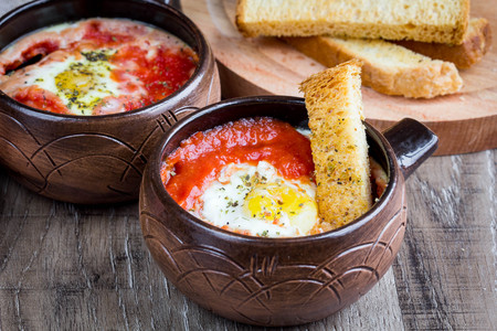 Egg baked in tomato sauce with bread croutons, toast, delicious Breakfast, healthy food in rustic styleの写真素材