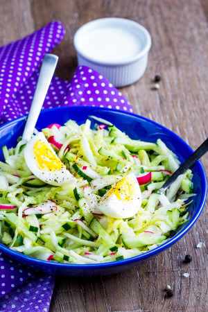 Fresh salad with cabbage, cucumber, radish and egg, healthy spring dish in rustic style and bright presentationの写真素材
