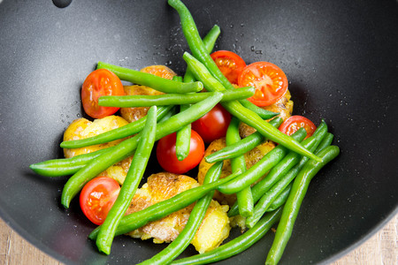 Roast vegetables in wok, potatoes, green beans, cherry tomatoes, sesame seeds, delicious vegetarian lunch on grillの写真素材
