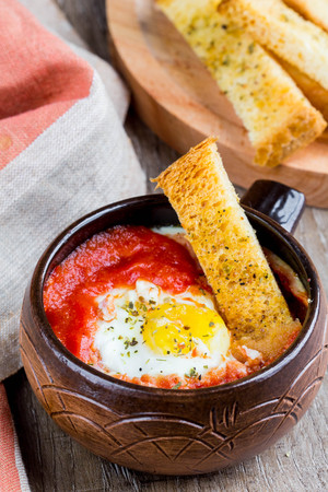 Egg baked in tomato sauce with bread croutons, toast, delicious Breakfast, healthy food in rustic styleの写真素材
