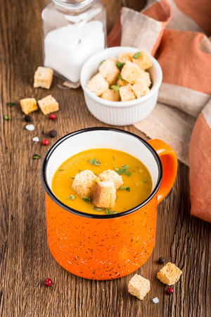 Orange cream soup in Ñup with croutons, carrot, pumpkin, delicious hot soup, homemade dinner in rustic styleの写真素材