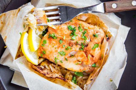 White fish fillet baked in parchment with rice and vegetables, delicious healthy dish, diet food