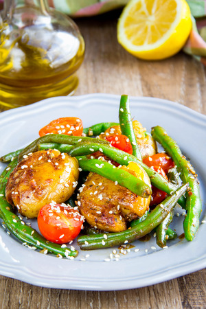 Roast vegetables in wok, potatoes, green beans, cherry tomatoes, sesame seeds, delicious vegetarian lunch on grillの写真素材
