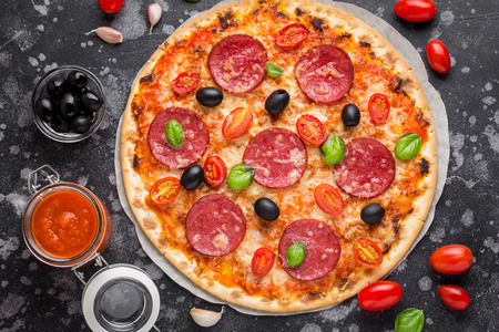 Italian pizza on thin dough with tomato sauce, salami, cheese, olives and Basilの写真素材