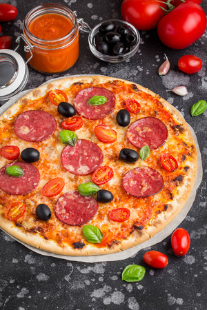 Italian pizza on thin dough with tomato sauce, salami, cheese, olives and Basilの写真素材