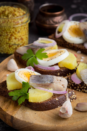 Sandwich on bread with herring, potatoes, egg, onion, tasty appetizer with mustard on the Boardの写真素材