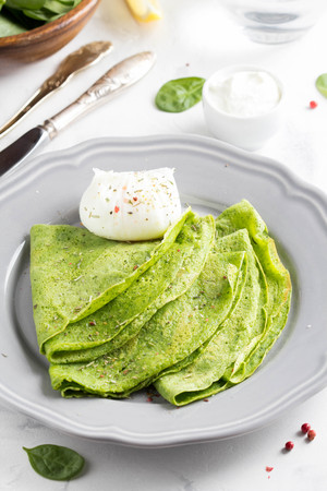 Green thin pancakes with spinach, poached egg, sour cream, lemon and aromatic herbs, delicious healthy food, Breakfastの写真素材