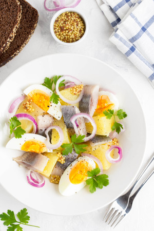 Potato salad with herring, egg, onion, tasty snack with mustard in a white plateの写真素材