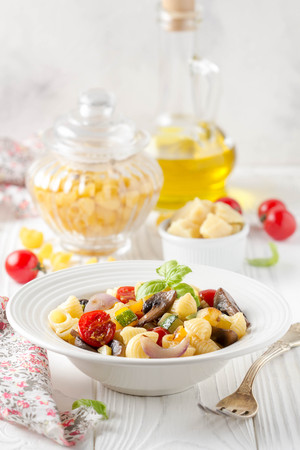 Italian pasta with fried vegetables and mushrooms, zucchini, cherry tomatoes, champignon, cheese, onion  and basil. White plateの写真素材