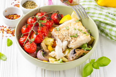 Baked vegetables with mushrooms and white fish fillets in a bowl. Zucchini, cherry tomatoes on a branch, red onions, bell peppers and garlic. Healthy diet foodの写真素材