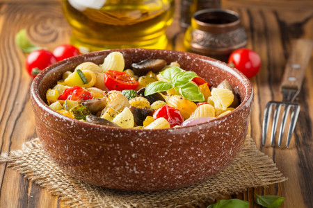 Italian pasta with fried vegetables and mushrooms, zucchini, cherry tomatoes, champignon, cheese and Basil. In dark bowl on a wooden backgroundの写真素材