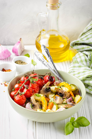 Baked vegetables with mushrooms in bowl. Zucchini, cherry tomatoes on a branch, red onions, bell peppers and garlic. Delicious garnish, vegetarian food, healthy dietの写真素材