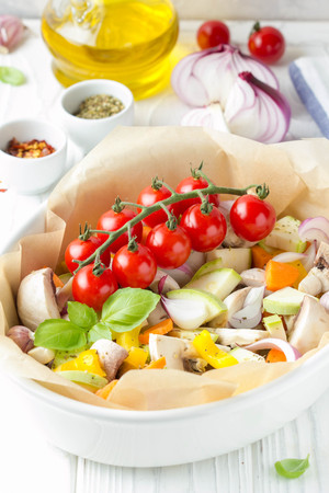 Preparation of baked vegetables with mushrooms in white. Zucchini, cherry tomatoes on a branch, red onions, bell peppers and garlic. Delicious garnish, vegetarian food, healthy dietの写真素材