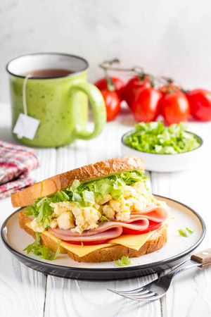 Ham sandwich with scrambled egg, cheese, tomato, lettuce, delicious healthy Breakfast on white wooden backgroundの写真素材