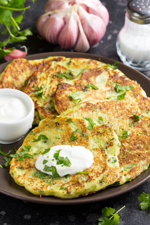 Zucchini pancakes with parsley, garlic and sour cream, summer food, delicious snack. In a dark plate on a dark backgroundの写真素材