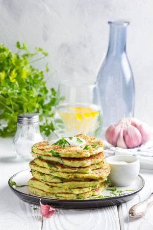 Zucchini pancakes with parsley and sour cream, summer food, delicious snack. High stack in a plate on white woodの写真素材