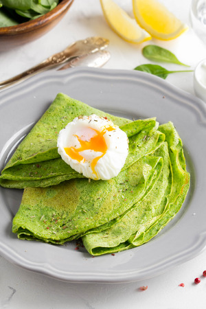 Green thin pancakes with spinach, poached egg, sour cream, lemon and aromatic herbs, delicious healthy food, Breakfastの写真素材