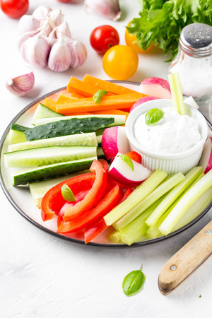 Tasty vegetable sticks of cucumber, pepper, carrots, celery and radishes with white sauce of sour cream, yogurt, herbs.の写真素材