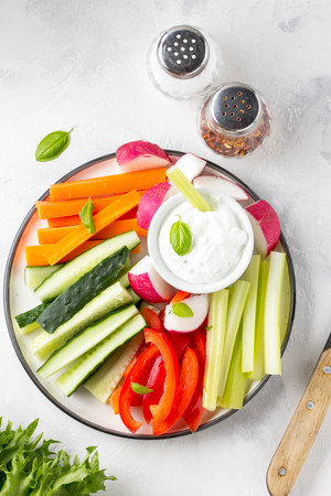 Tasty vegetable sticks of cucumber, pepper, carrots, celery and radishes with white sauce of sour cream, yogurt, herbs.の写真素材