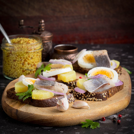 Sandwich on bread with herring, potatoes, egg, onion, tasty appetizer with mustard on the Boardの写真素材