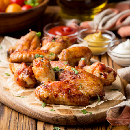 Grilled chicken wings with ketchup and mustard sauces on a wooden board. Traditional baked bbq buffaloの写真素材