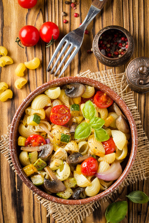 Italian pasta with fried vegetables and mushrooms, zucchini, cherry tomatoes, champignon, cheese and Basil. In dark bowl on a wooden backgroundの写真素材