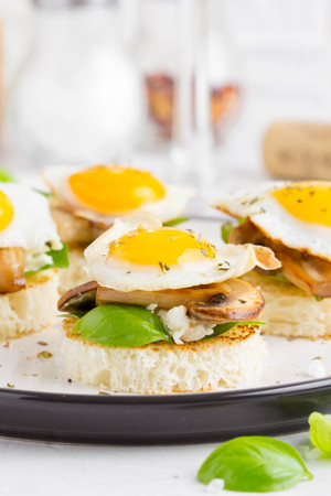 Canapes with fried mushrooms, quail egg, soft cheese and basil, beautiful appetizer for home party or event, tasty breakfastの写真素材
