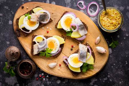 Sandwich on bread with herring, potatoes, egg, onion, tasty appetizer with mustard on the Boardの写真素材