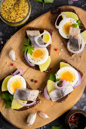 Sandwich on bread with herring, potatoes, egg, onion, tasty appetizer with mustard on the Boardの写真素材