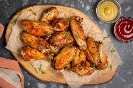 Grilled chicken wings with ketchup and mustard sauces on a wooden board. Traditional baked bbq buffaloの写真素材