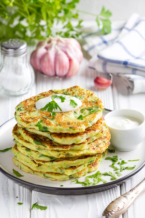 Zucchini pancakes with parsley and sour cream, summer food, delicious snack. High stack in a plate on white woodの写真素材