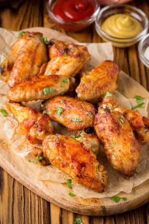 Grilled chicken wings with ketchup and mustard sauces on a wooden board. Traditional baked bbq buffaloの写真素材