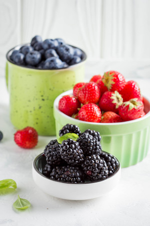 Fresh blueberries, strawberries, blackberries in cups, juicy summer berry on a light background, home harvest, gardenの写真素材
