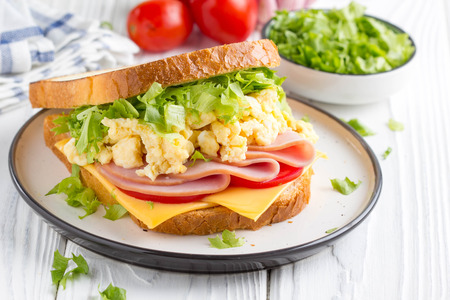 Ham sandwich with scrambled egg, cheese, tomato, lettuce, delicious healthy Breakfast on white wooden backgroundの写真素材