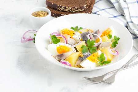 Potato salad with herring, egg, onion, tasty snack with mustard in a white plateの写真素材