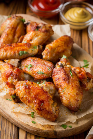 Grilled chicken wings with ketchup and mustard sauces on a wooden board. Traditional baked bbq buffaloの写真素材