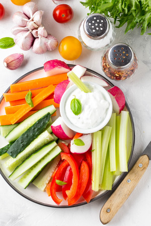Tasty vegetable sticks of cucumber, pepper, carrots, celery and radishes with white sauce of sour cream, yogurt, herbs.の写真素材