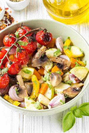 Baked vegetables with mushrooms in bowl. Zucchini, cherry tomatoes on a branch, red onions, bell peppers and garlic. Delicious garnish, vegetarian food, healthy dietの写真素材