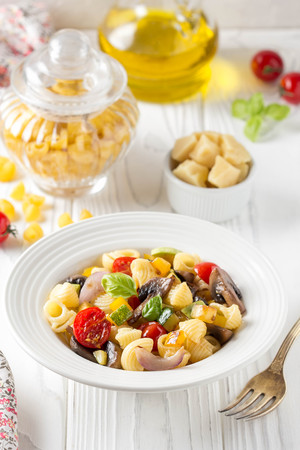 Italian pasta with fried vegetables and mushrooms, zucchini, cherry tomatoes, champignon, cheese, onion  and basil. White plateの写真素材
