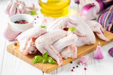 Raw chicken wings on a cutting board. Ingredients for cooking, spices, onion, oil and garlicの写真素材