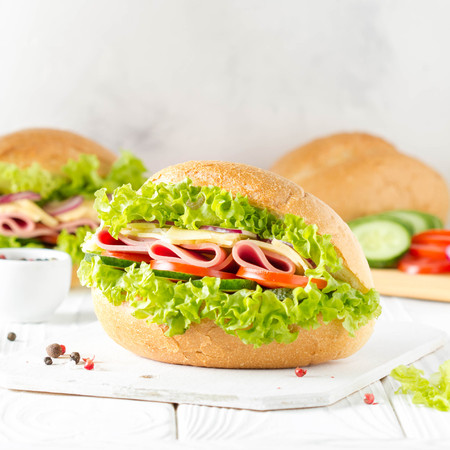 Closed sandwich in a bun with ham, cheese, lettuce, tomato, cucumber, red onion. Delicious breakfast, classic lunchの写真素材