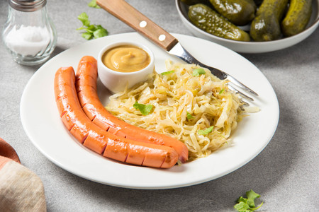 Stewed white cabbage with two long fried sausages, mustard and pickled cucumbers.の写真素材