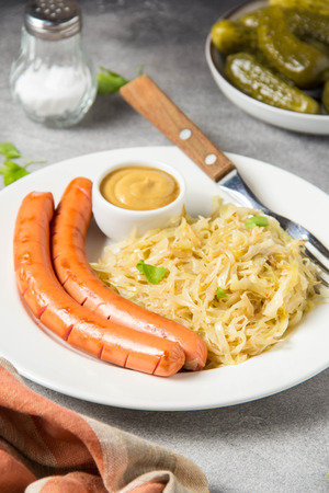 Stewed white cabbage with two long fried sausages, mustard and pickled cucumbers.の写真素材