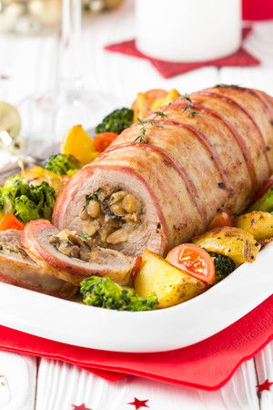 Pork roll wrapped in bacon stuffed with mushrooms and beans, vegetables on the side. Beautiful festive main dish for the Christmas holidaysの写真素材