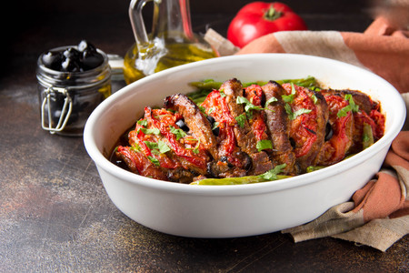 Baked whole pork meat with tomatoes, green beans and black olivesの写真素材