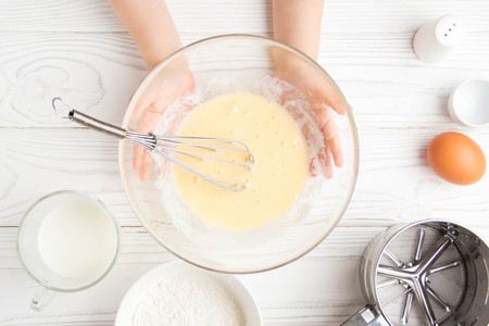 Children's small hands beat the dough for pancakes cooking in the kitchenの写真素材