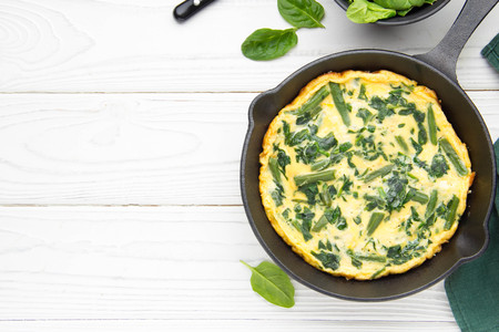 Omelet with spinach and green beans, healthy food. Egg and milk Frittata, delicious Breakfast. In black frying pan on white wooden background with copyspaceの写真素材