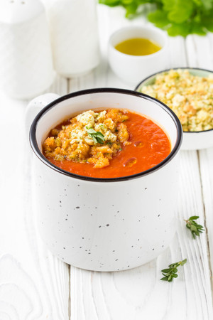 Tomato cream soup in white mug, red hot soup in cup with fragrant breadcrumbs and olive oil. Vegetarian vegetable lunch on wooden backgroundの写真素材